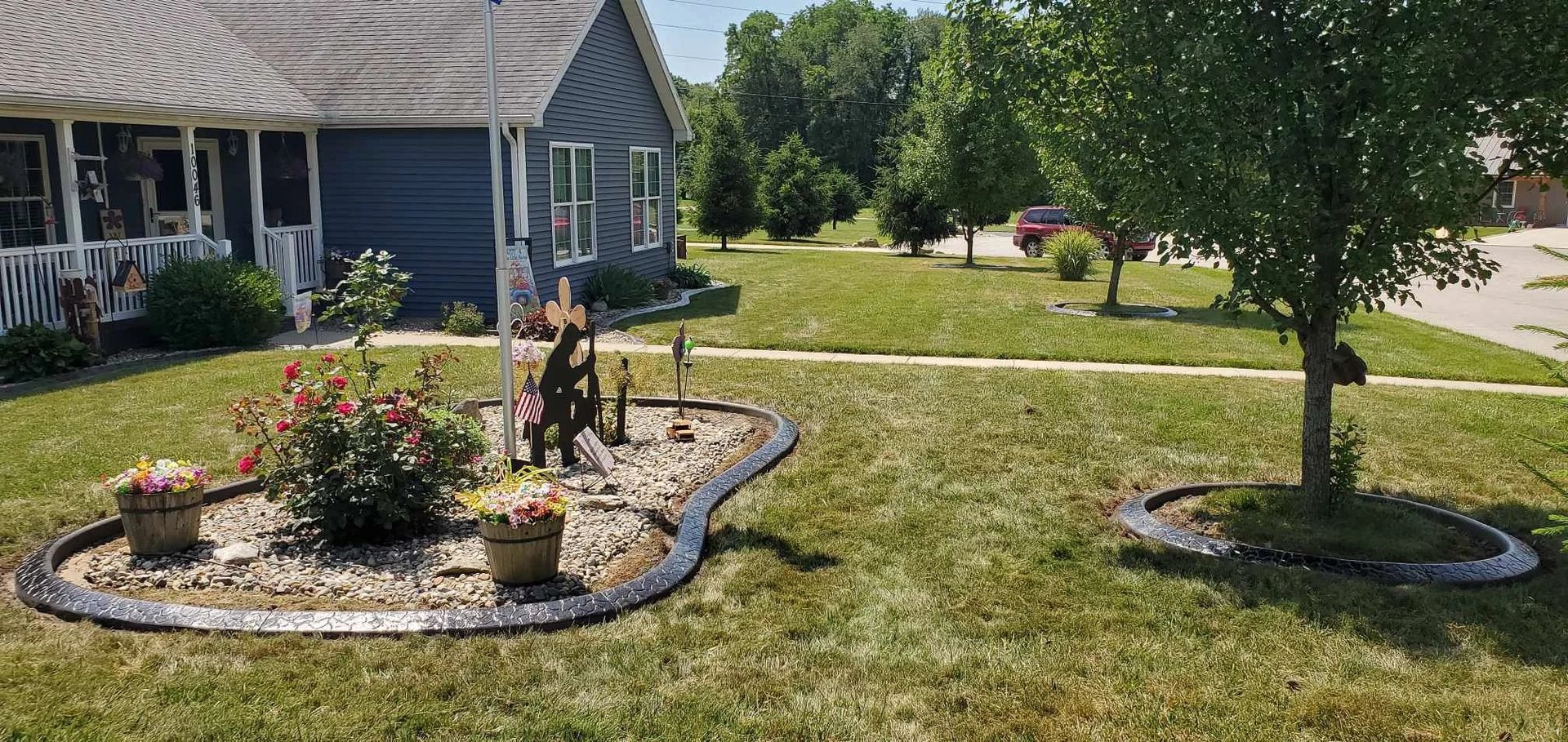 A house with a blue exterior and a decorative flower bed in front. Green trees and grass surround it.