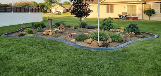 A landscaped flower bed with dark edging surrounded by green grass in a backyard.