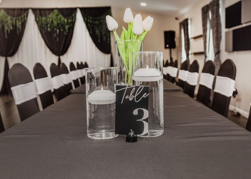 Rows of black chairs with gold sashes in a white banquet hall with dark wood floors