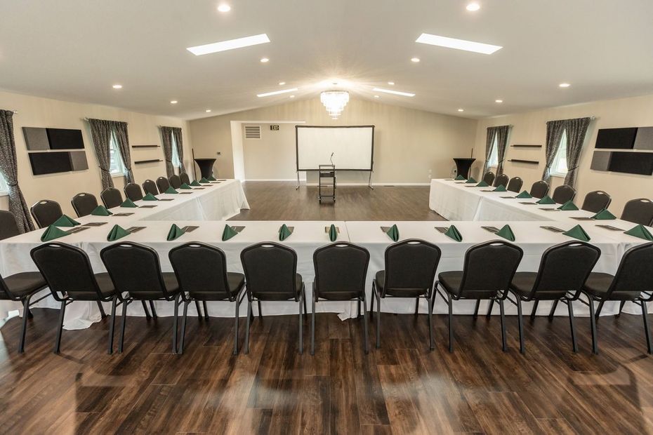 Banquet hall set up with black-covered tables and chairs, wood floor, and a projected presentation screen.