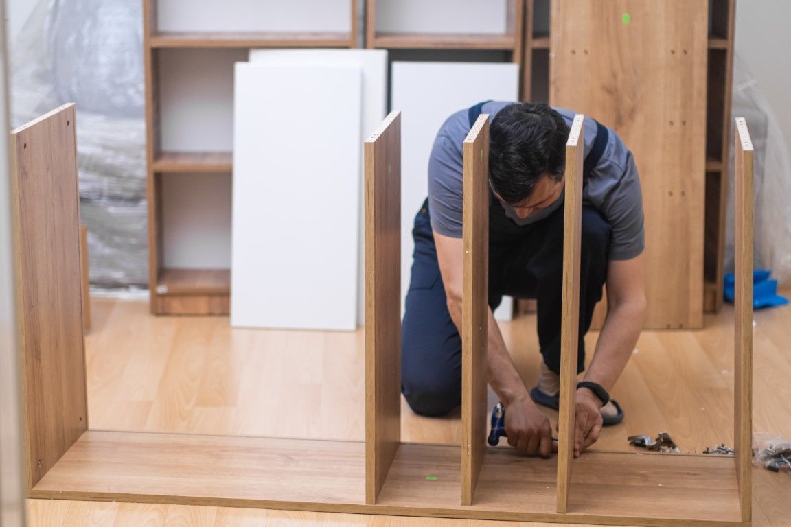 Person assembling a wooden cabinet frame on a floor in a workshop-like room