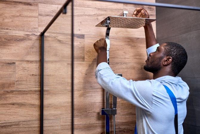 Person installing a shelf bracket on a wooden wall with a drill stand nearby