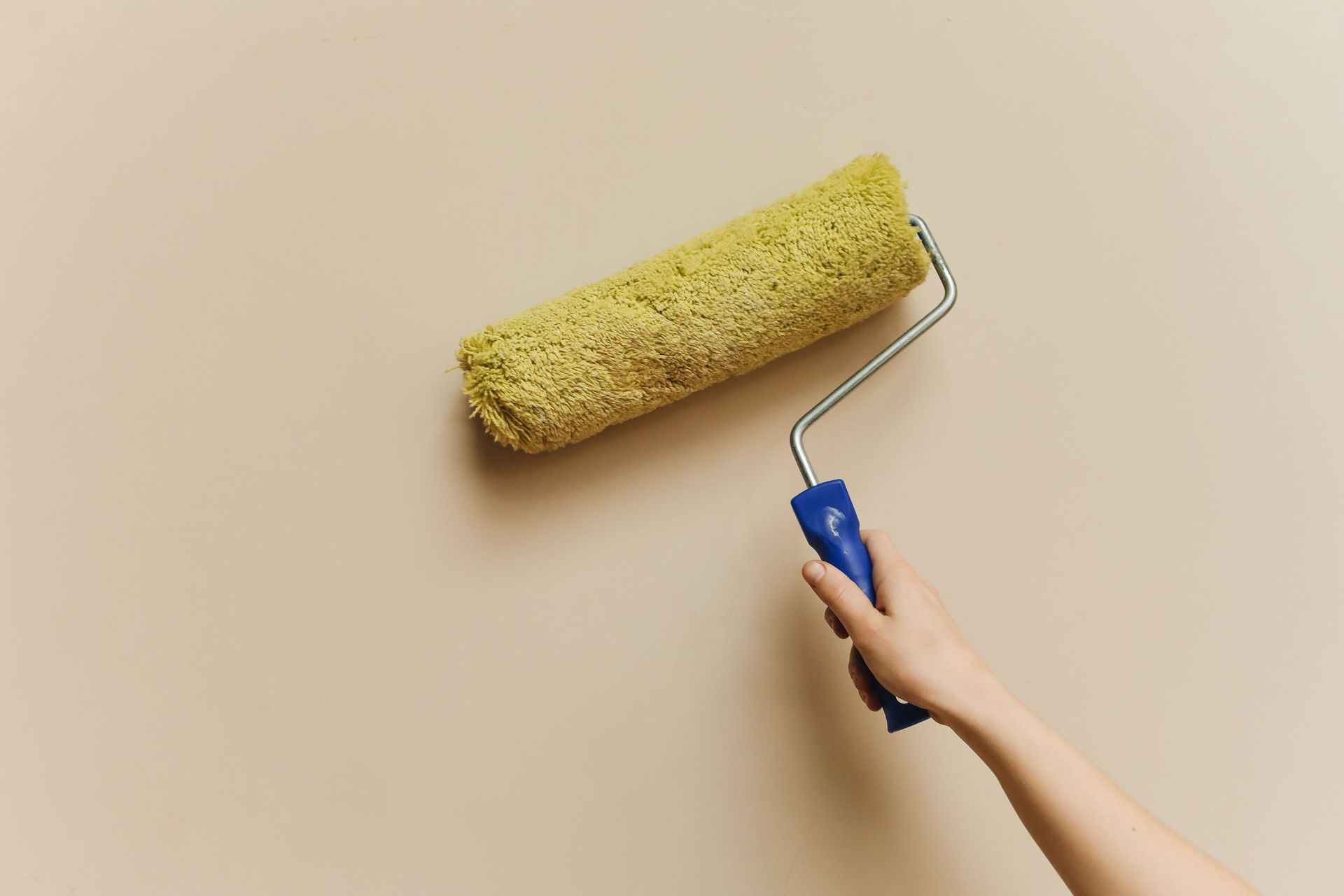 Hand using a blue roller to paint a beige wall yellow