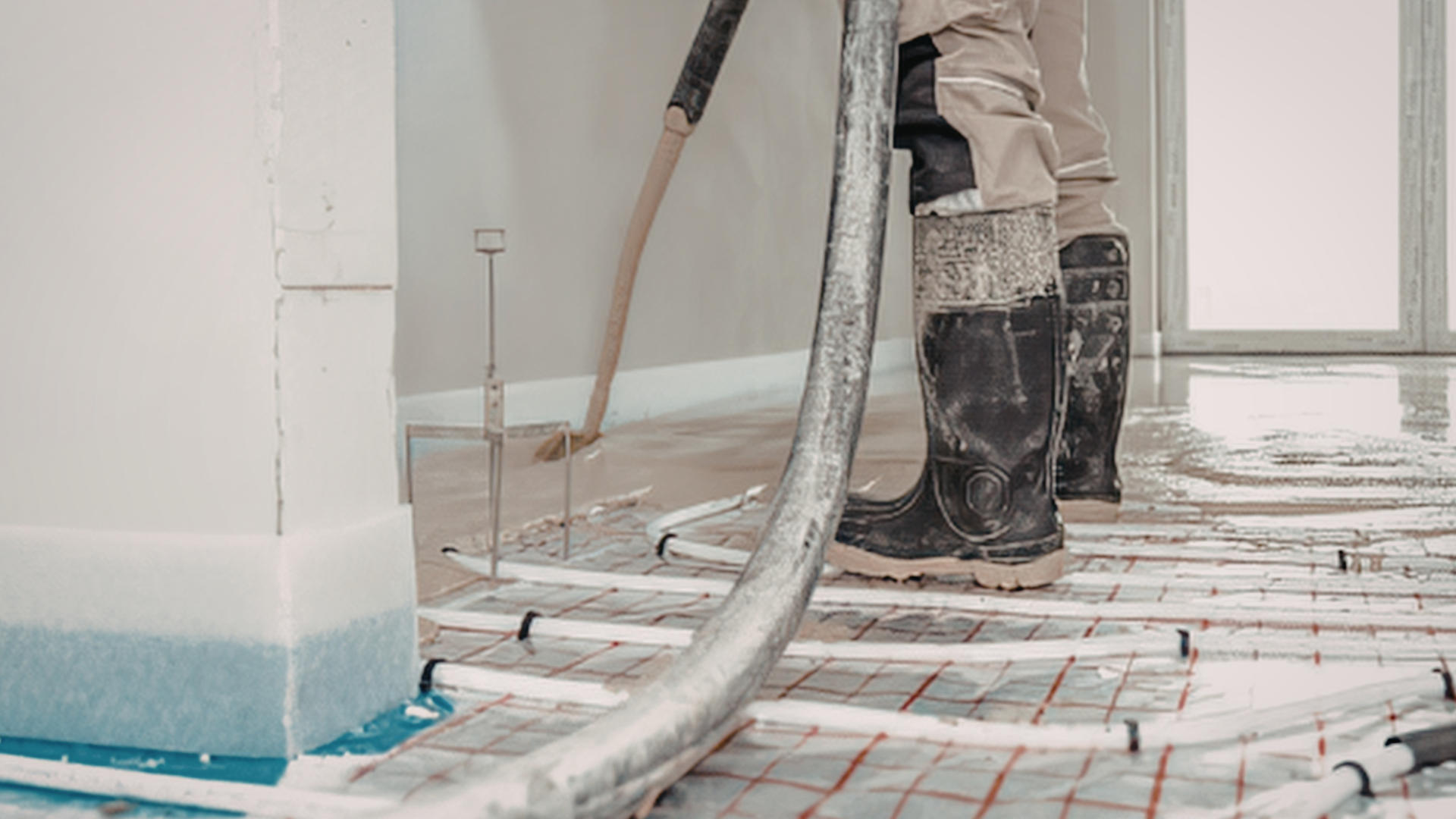 Worker in boots standing on a tiled floor during home renovation, with hoses and insulation visible.