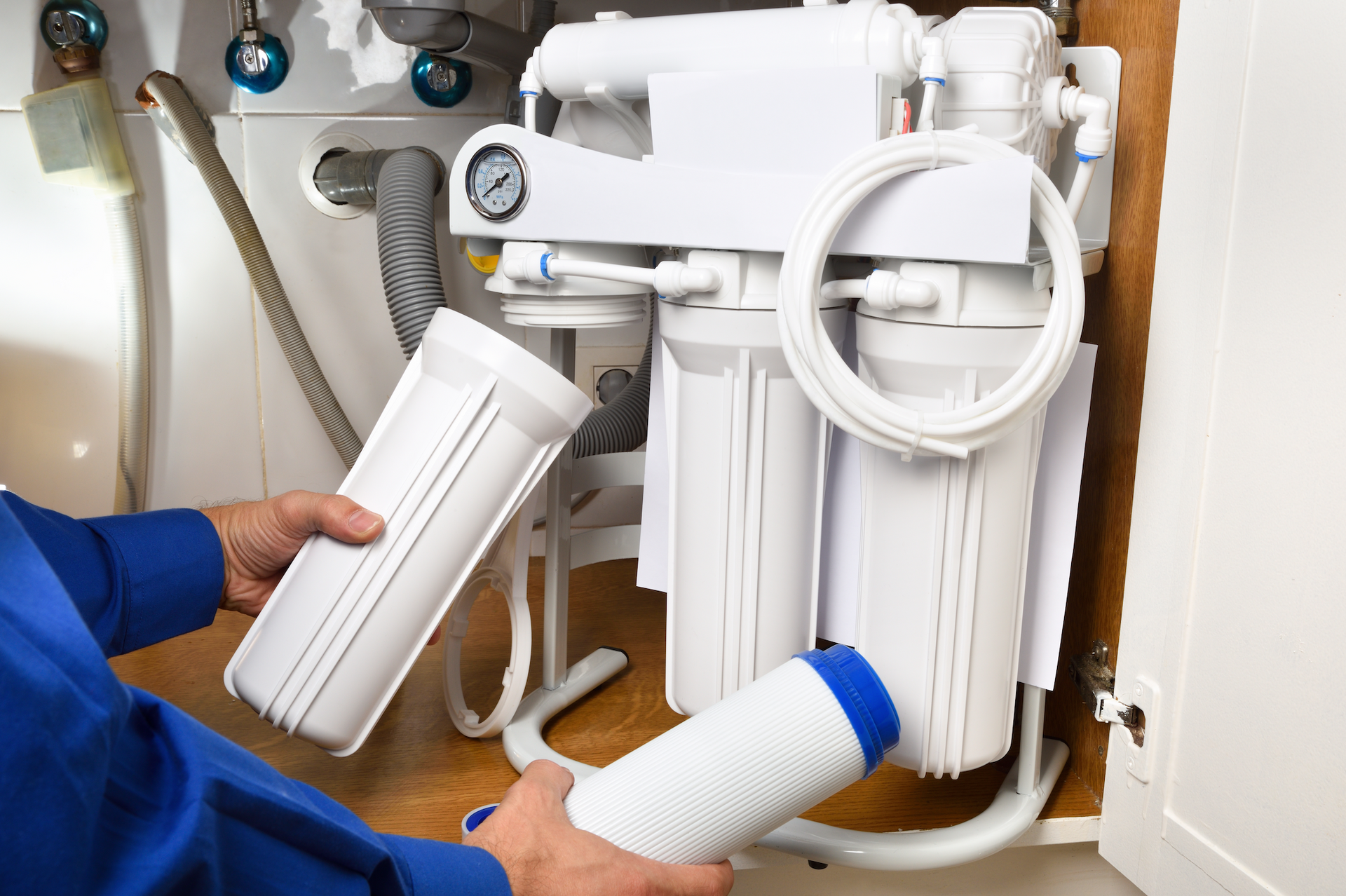 A man is fixing a water filter under a sink.