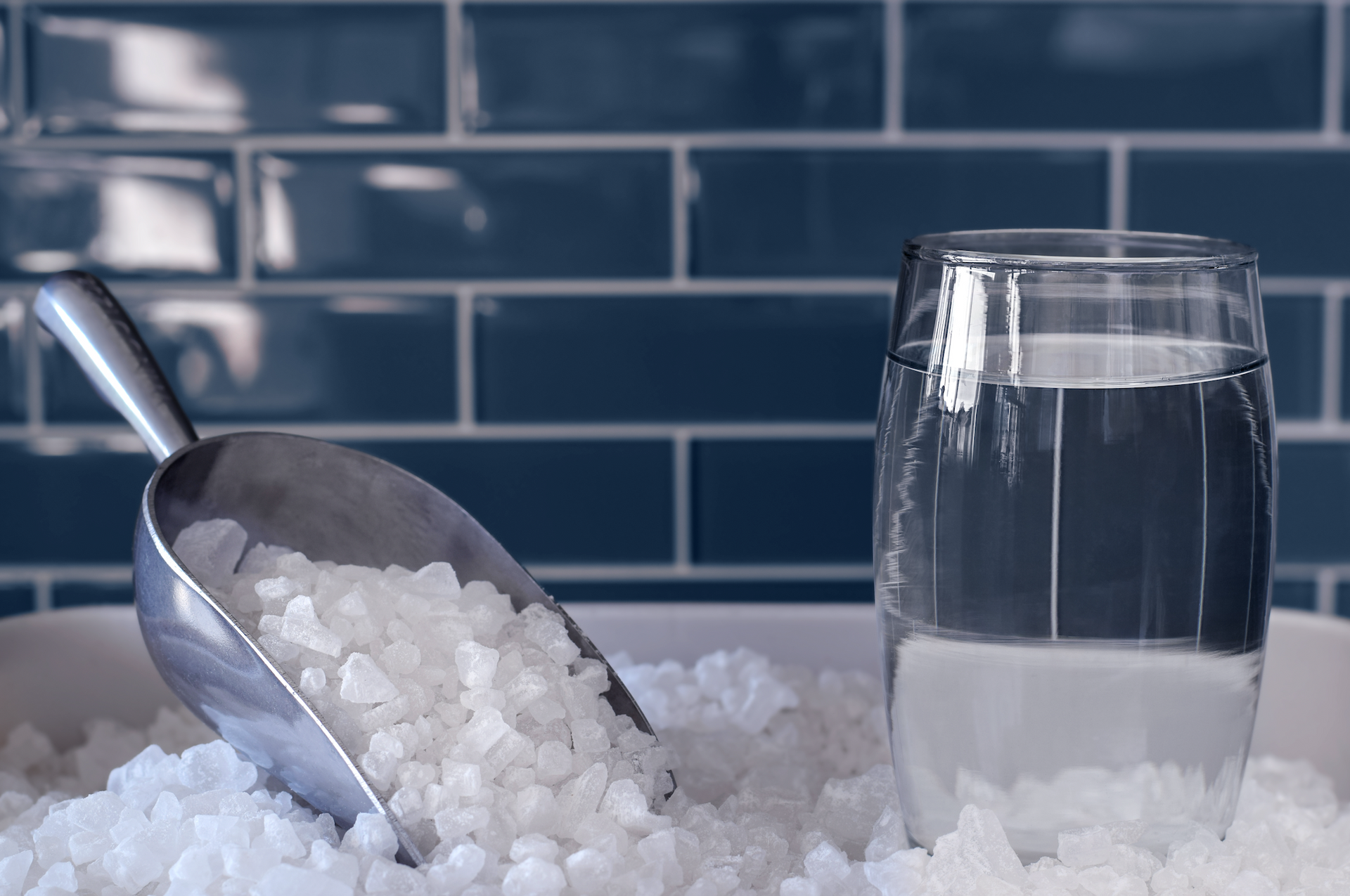 A scoop of salt next to a glass of water.