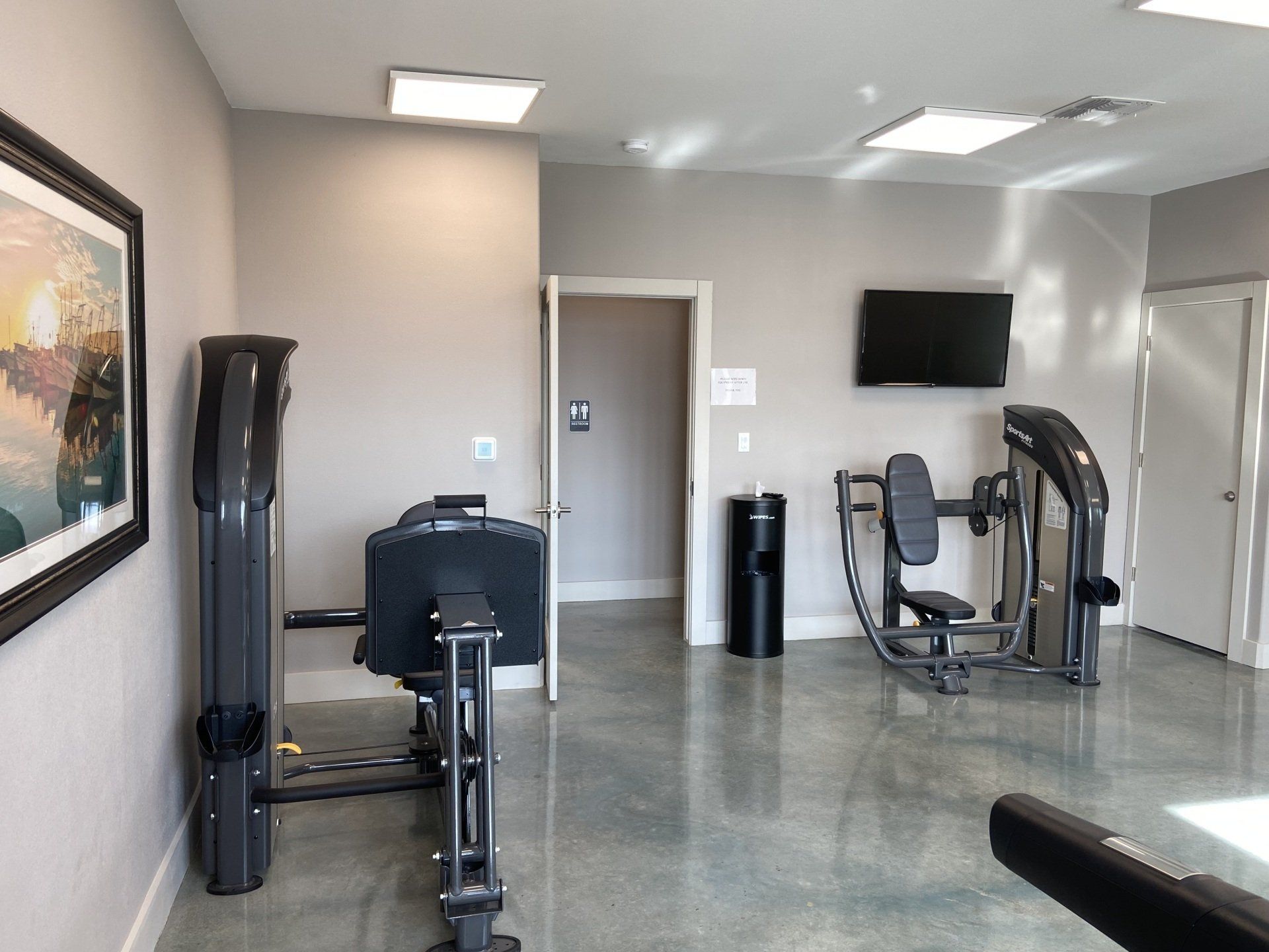 A gym with a lot of exercise equipment and a television on the wall.