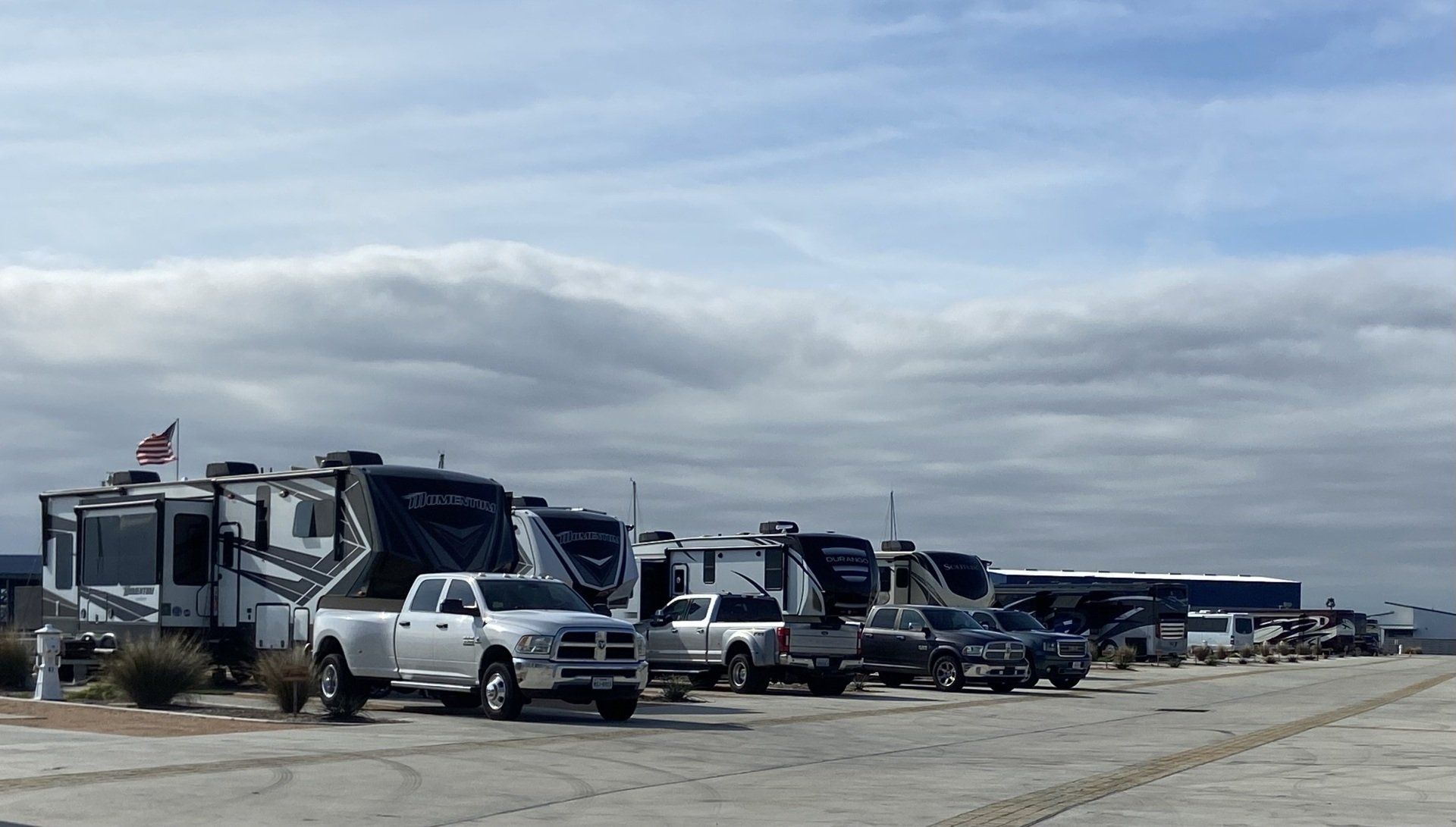 A row of rvs and trucks are parked in a parking lot.