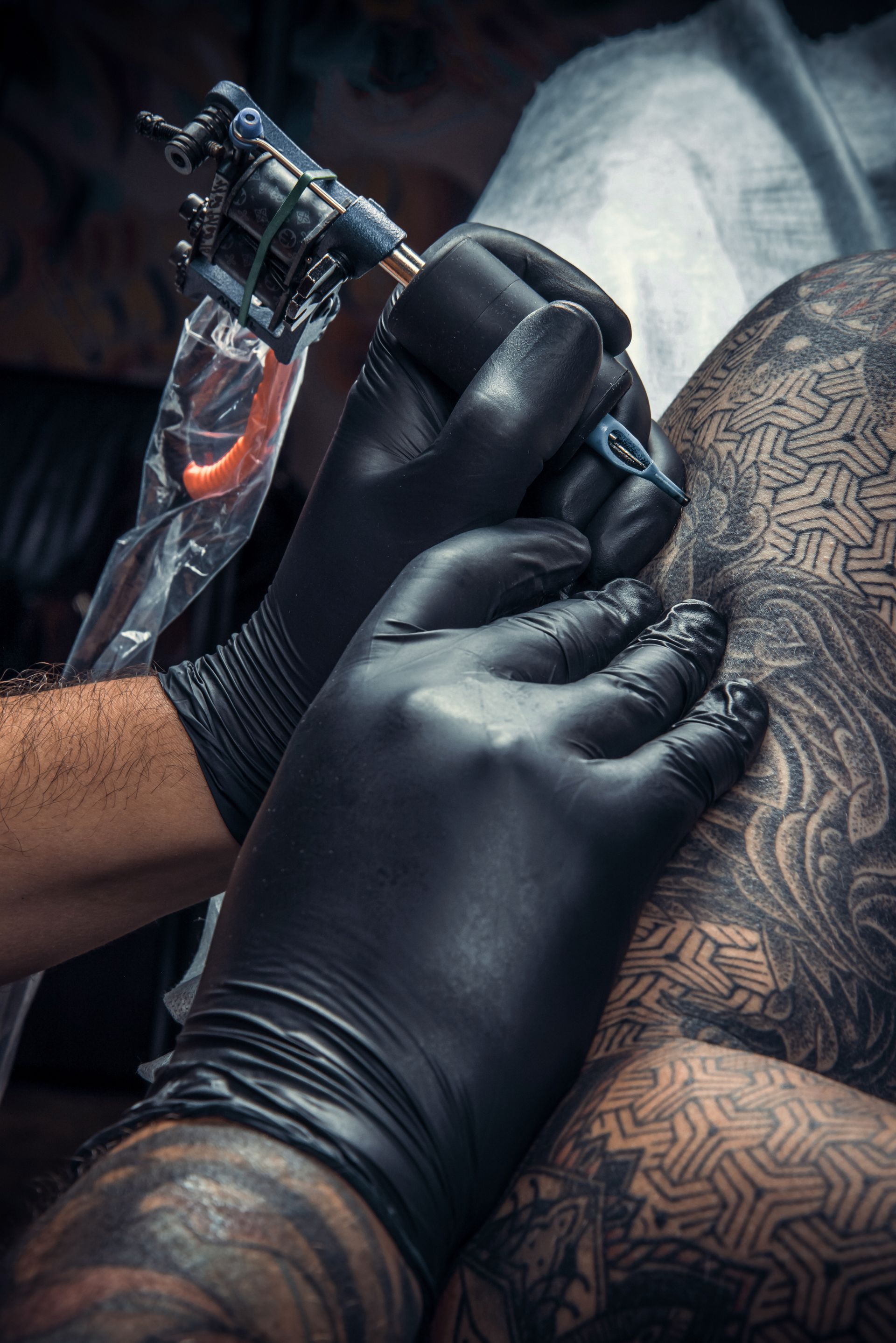 Gloved hands tattooing a person’s shoulder with a tattoo machine