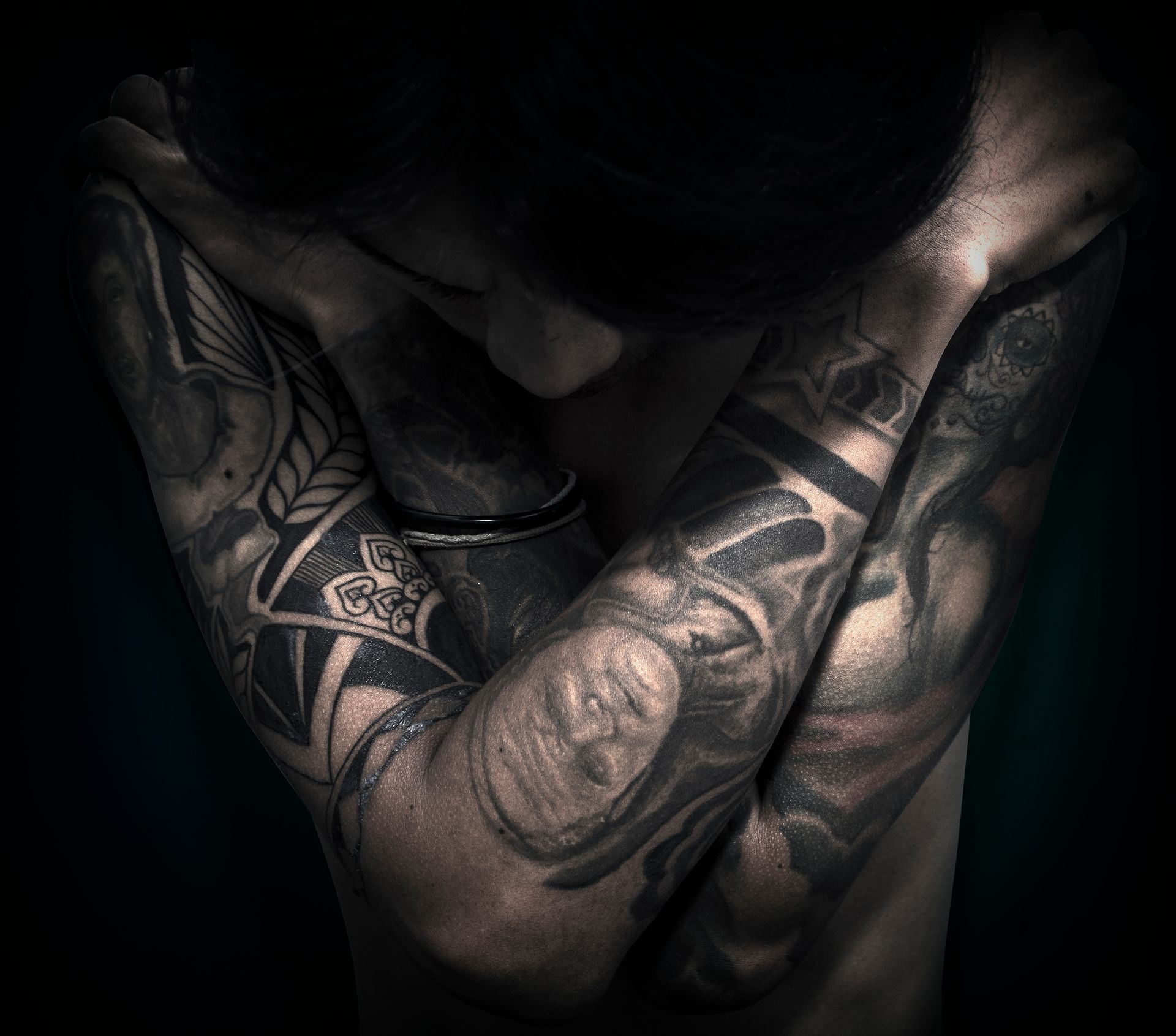 Tattooed forearms crossed over a bare chest in dramatic low light