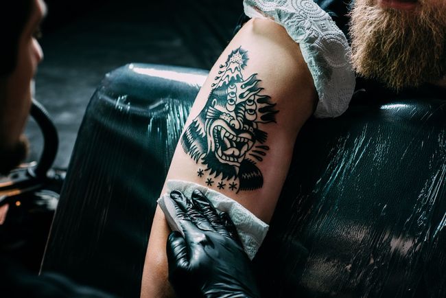 Tattoo artist working on a black-and-white arm tattoo in a studio