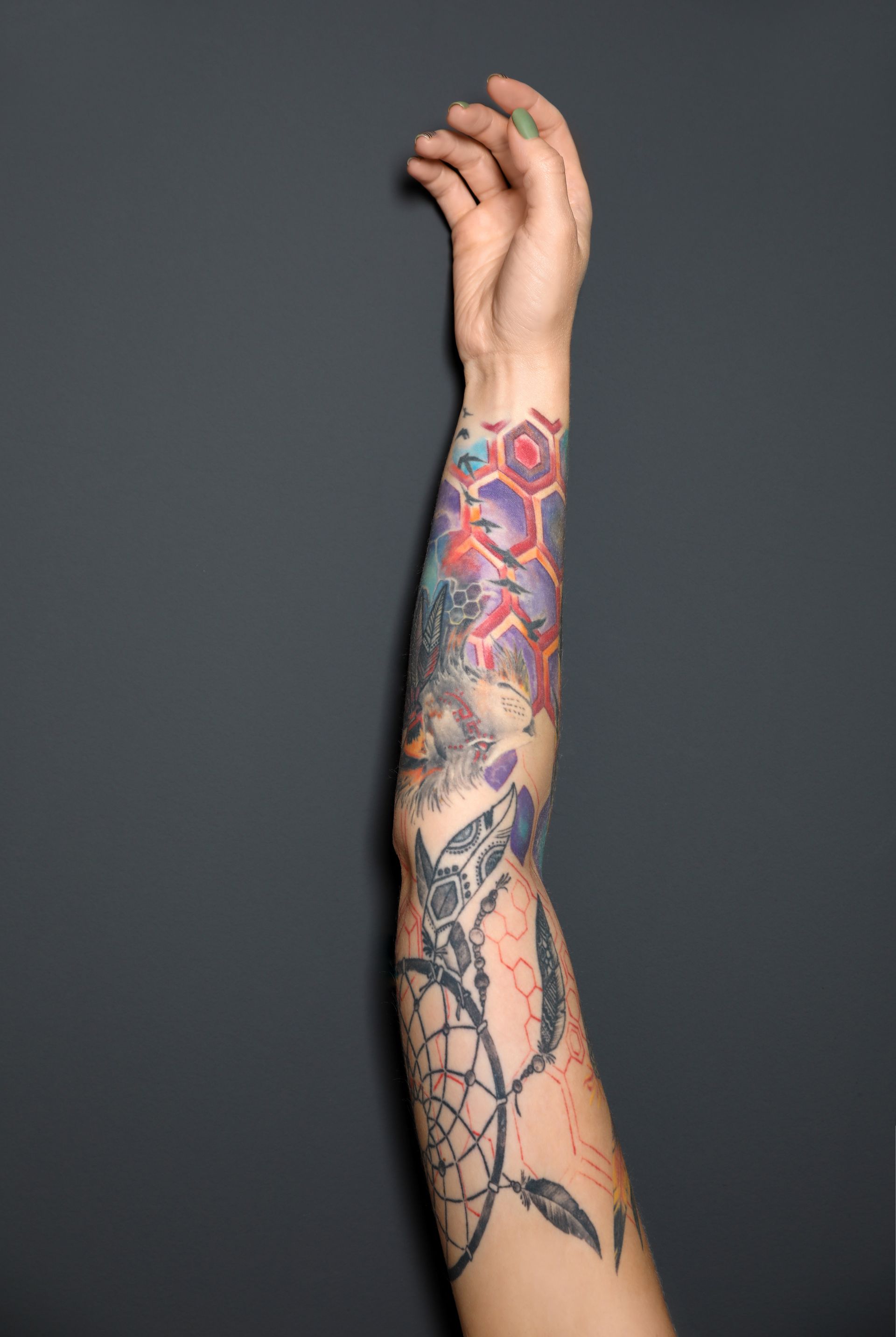Tattooed forearm raised against a dark gray background, showing colorful geometric and floral ink
