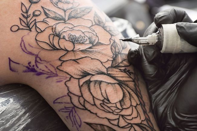 Tattoo artist outlining a floral design on skin with a black-gloved hand and tattoo machine