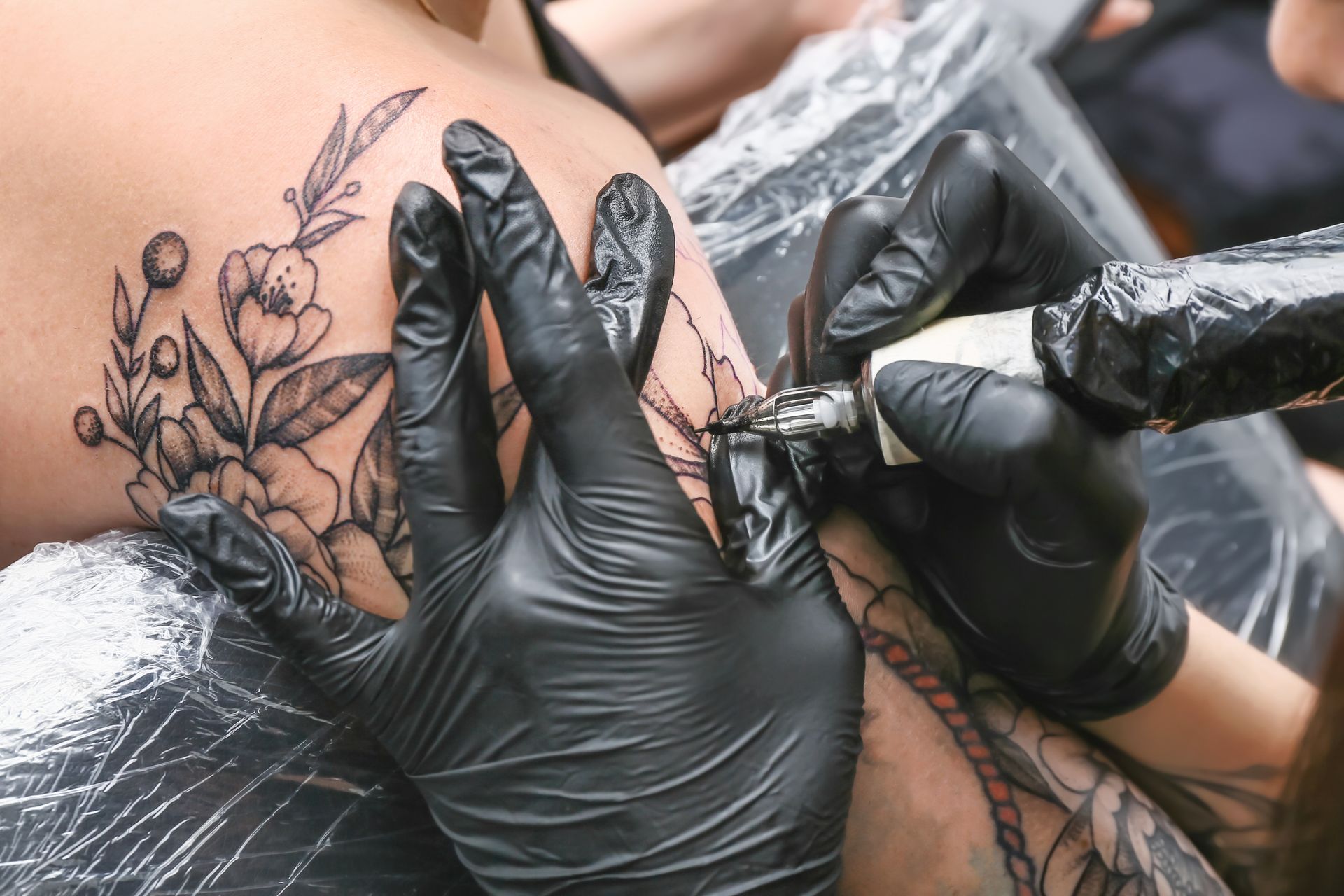 Tattoo artist wearing black gloves inks a floral tattoo on skin with a needle