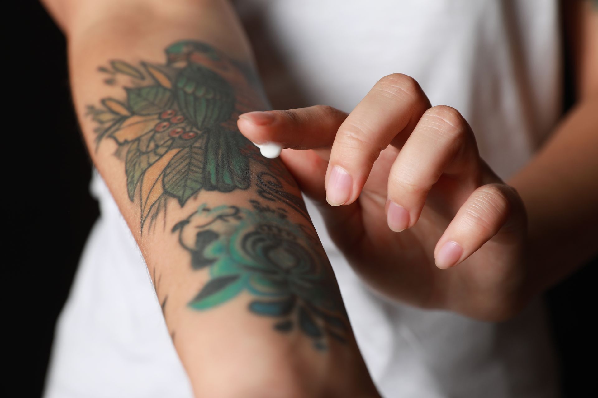 A hand touches a tattooed forearm with green leaf and blue designs.