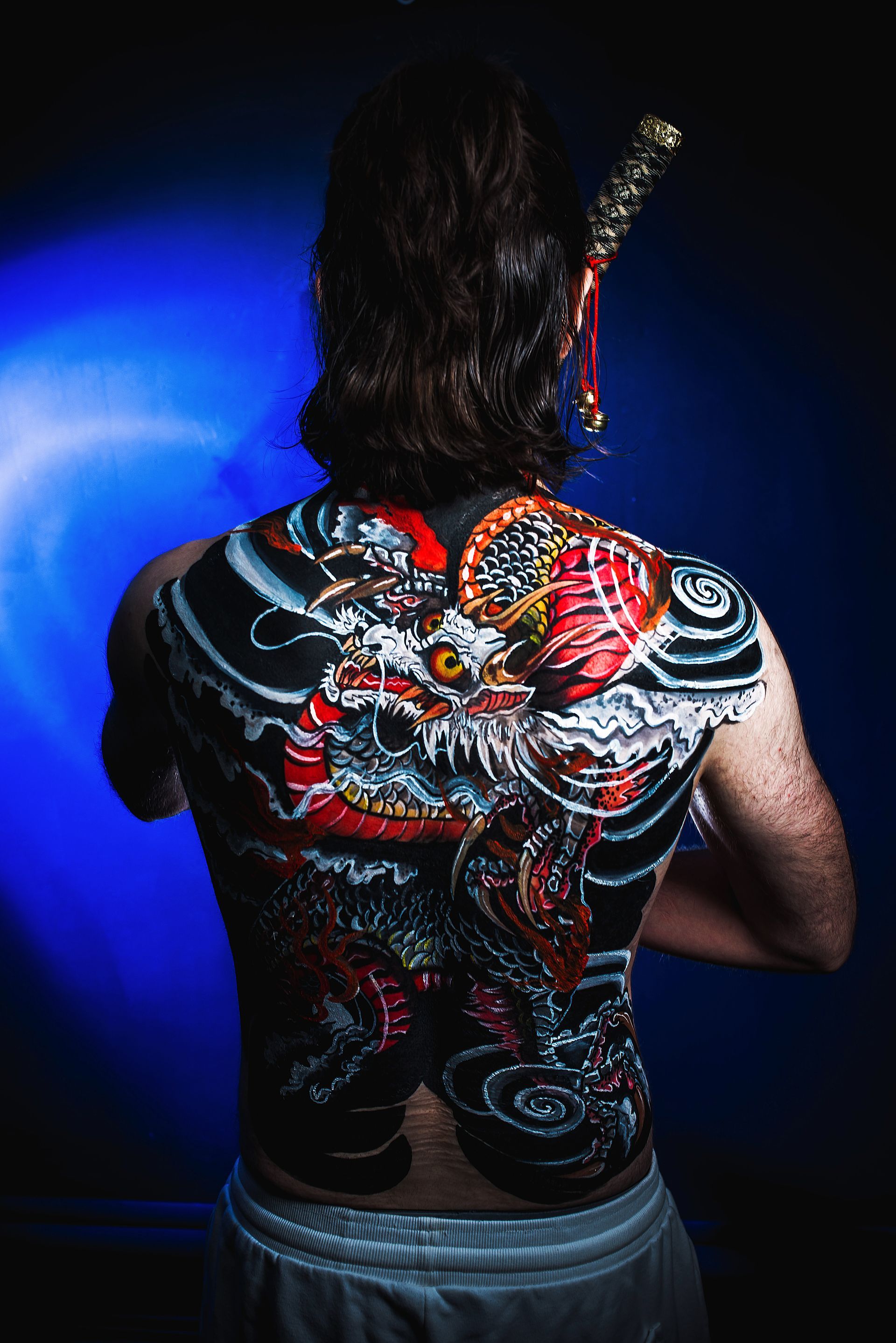 Person with dragon back tattoo and guitar against a dark blue-lit background
