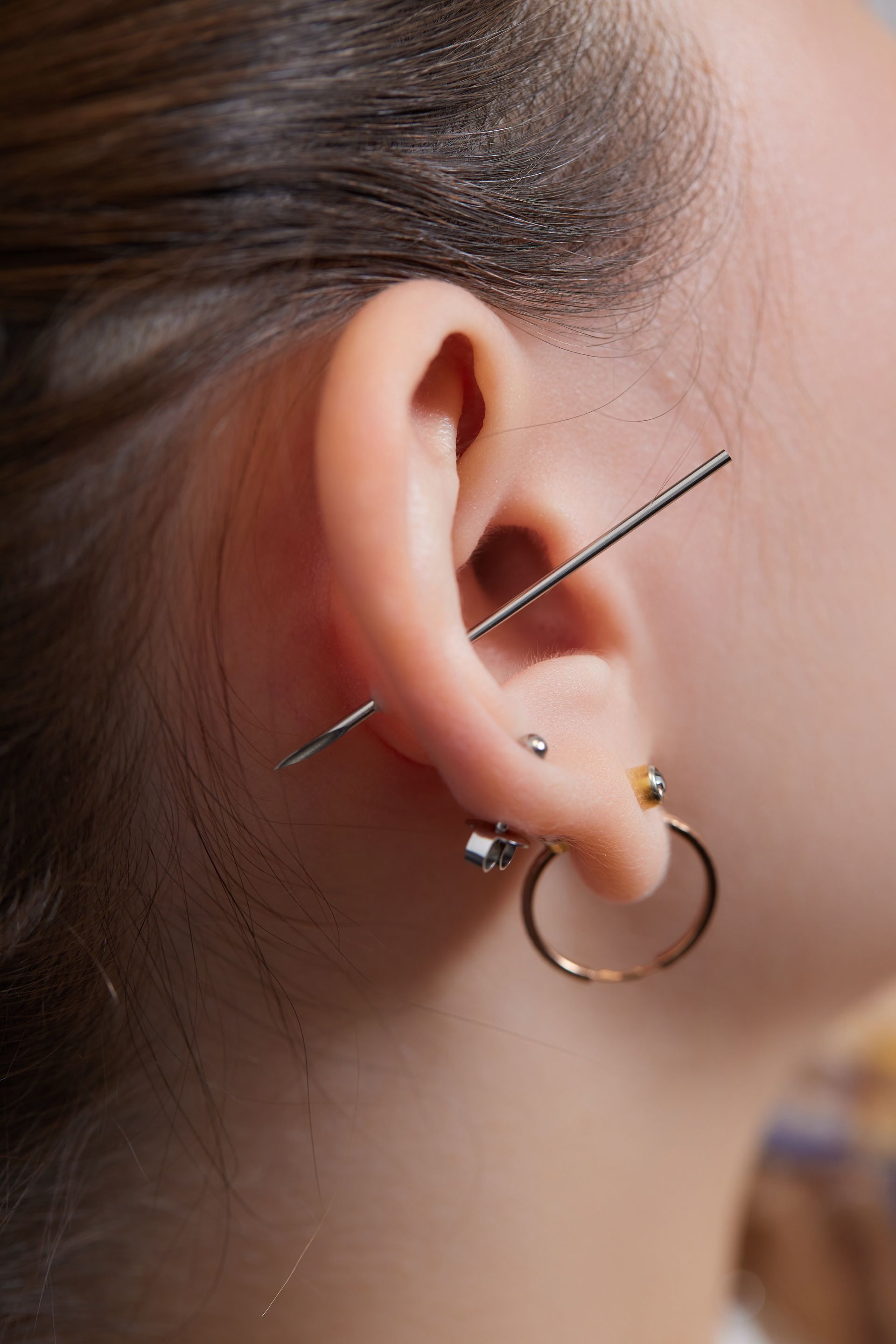 Close-up of a woman’s ear with multiple piercings and a thin needle passing through one piercing