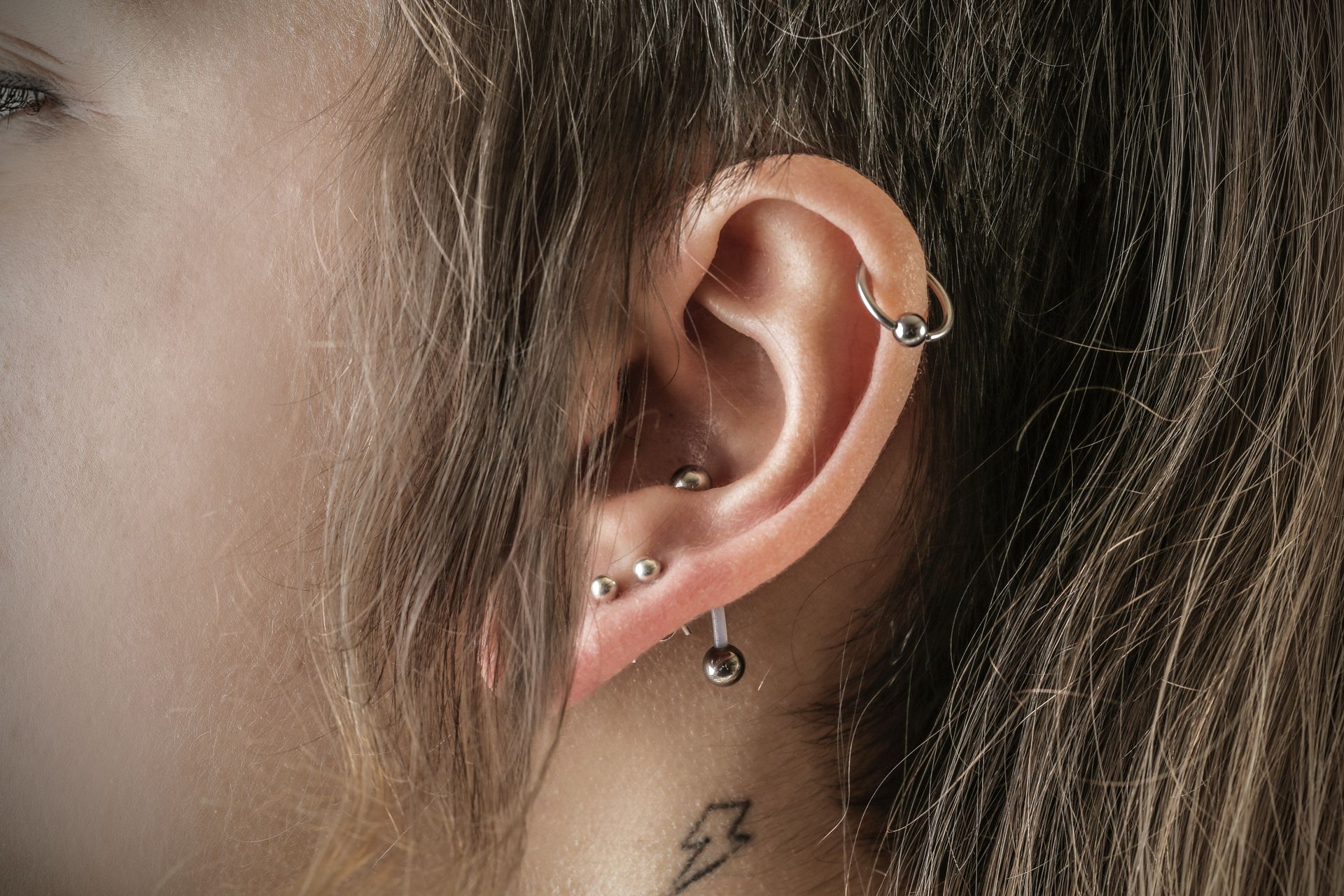Close-up of an ear with multiple silver piercings and a small neck tattoo