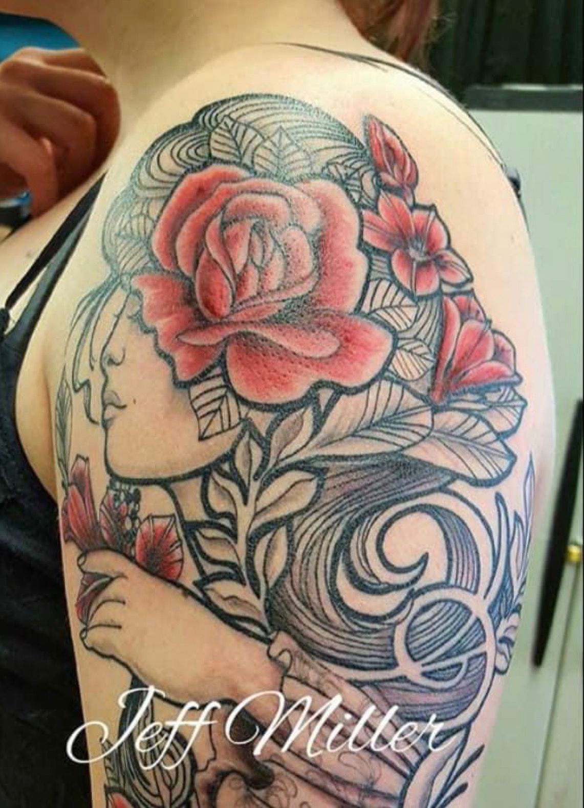 Tattoo of a black and orange eagle perched over a skull with red handprints and flowers on an arm