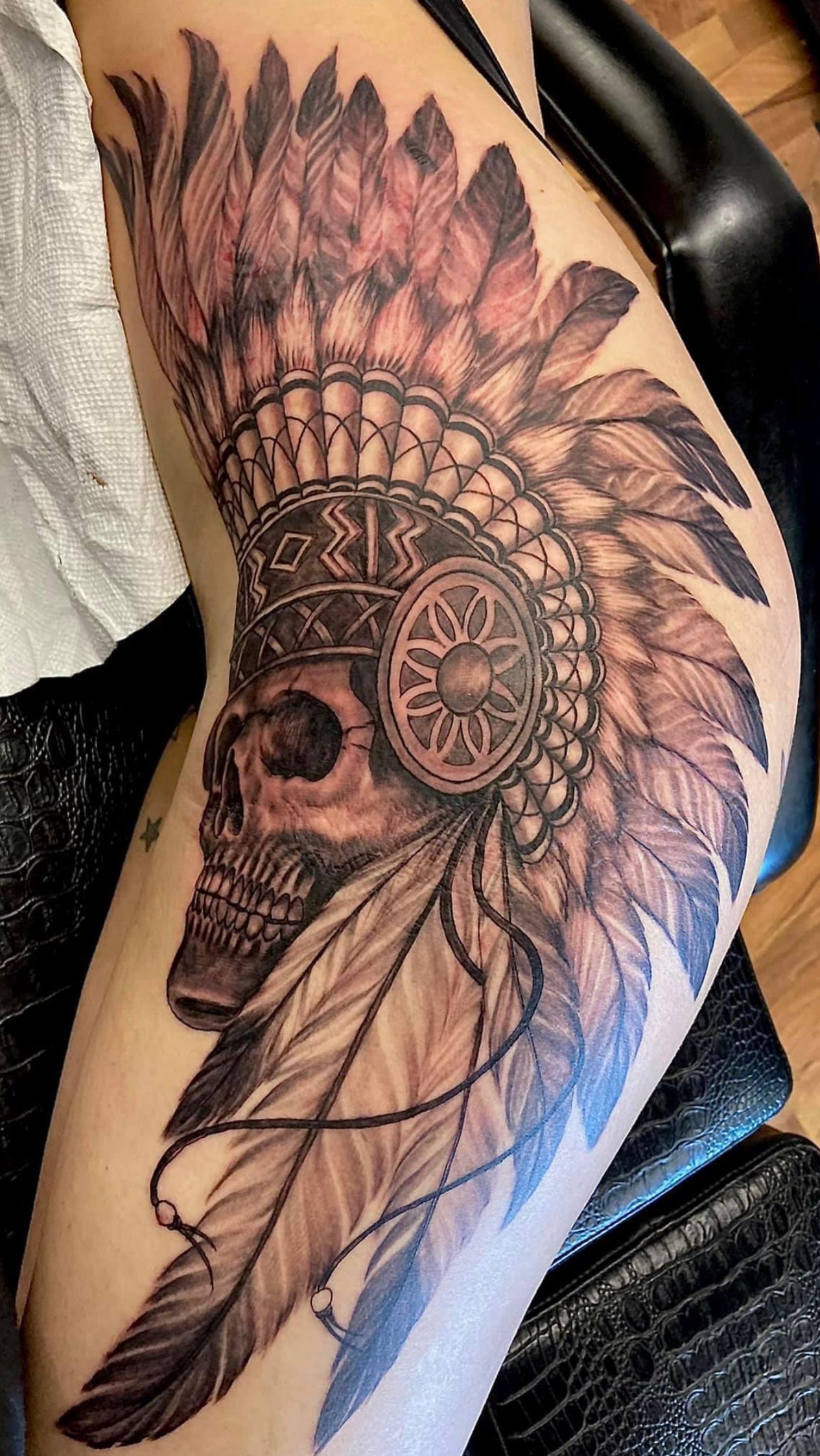 A hand touches a tattooed forearm with green leaf and blue designs.