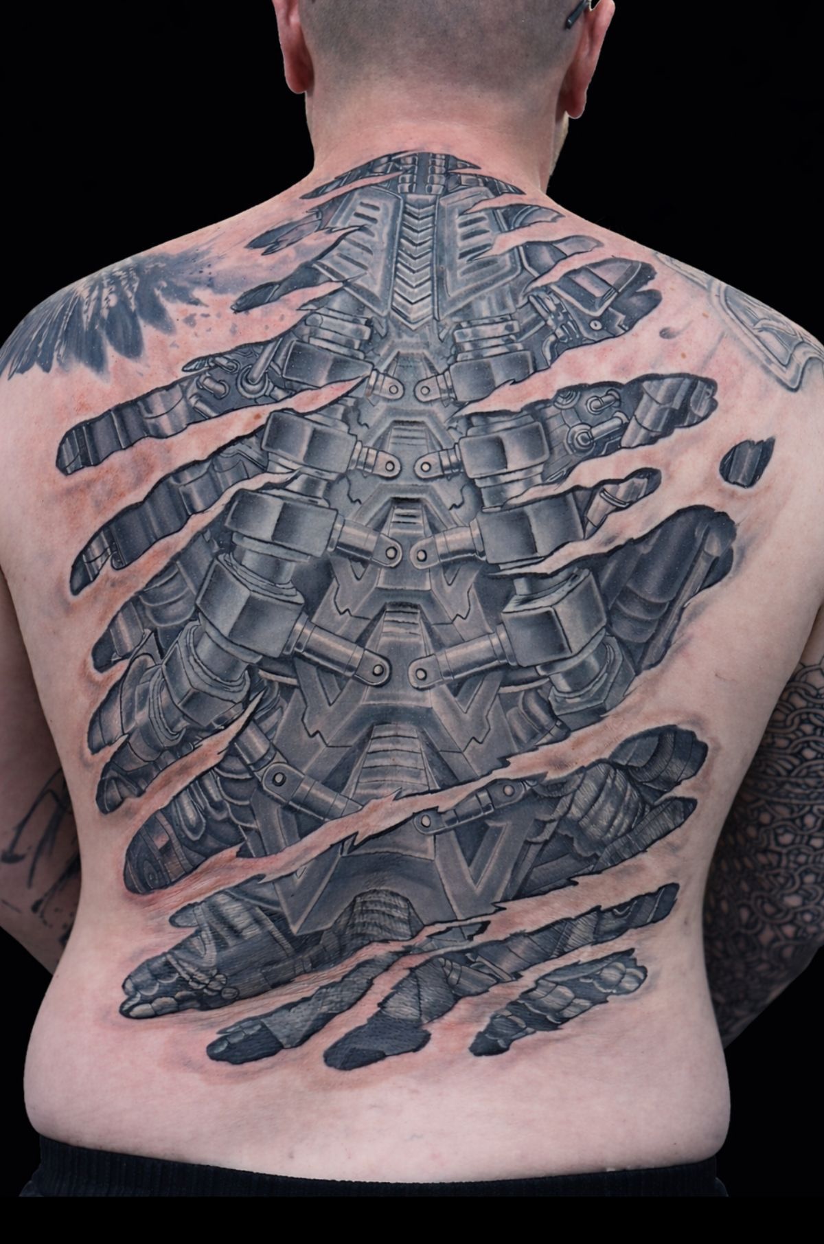 Back view of a person with a large black and gray biomechanical tattoo across the entire back