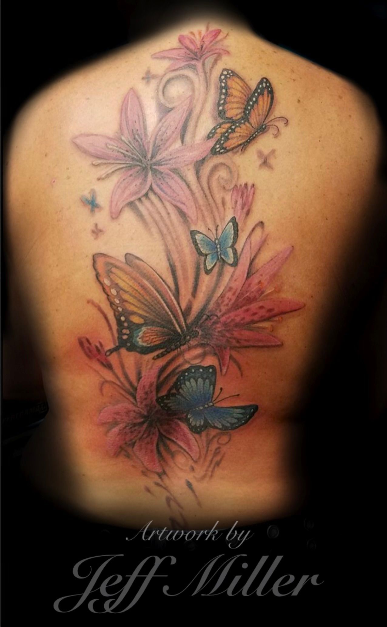 Colorful butterfly and flower tattoo on a person's upper back and shoulder with pink, teal, and black details