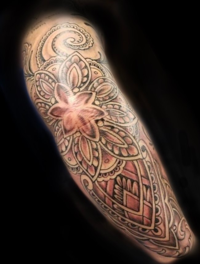 Tattoo artist in gloves tattooing a client’s forearm under a bright lamp