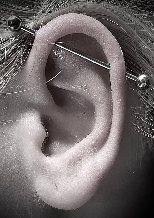 Gloved hands adjust an ear piercing on a person with a bandaged head.