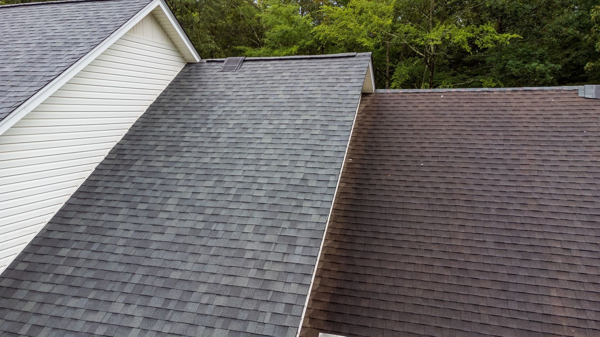 A dark gray and brown shingled roof next to a white sided house.