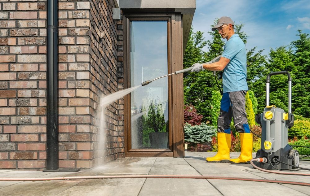 Person pressure-washing a brick house entryway with a hose and yellow boots