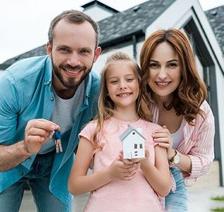 Smiling family holding a small house model in front of a new home under construction