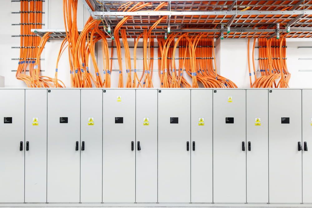 Rows of Gray Electrical Cabinets With Orange Cables Overhead — Darwin Electrical Services in Rural & Remote, NT