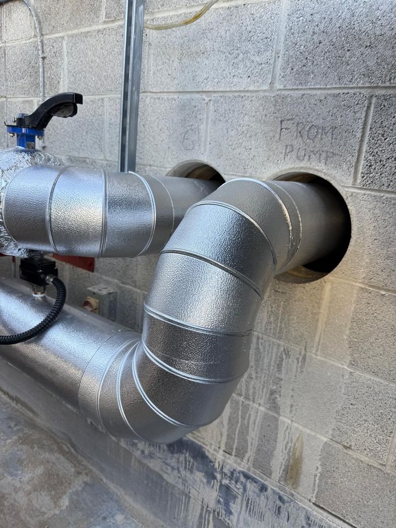 Insulated metal pipes with a black valve against a gray cinder block wall