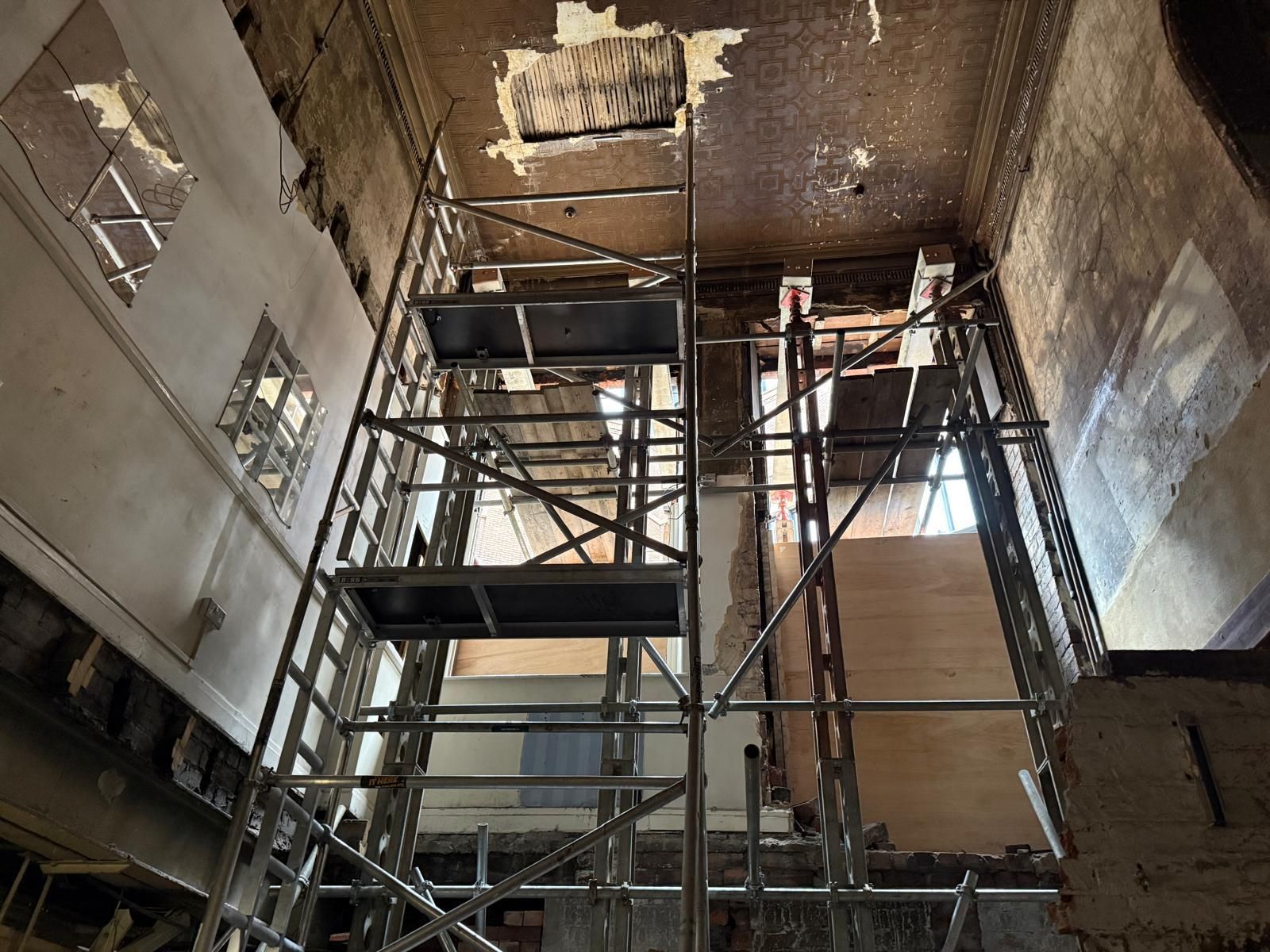 Scaffolding inside a damaged building with exposed ceiling and walls under repair