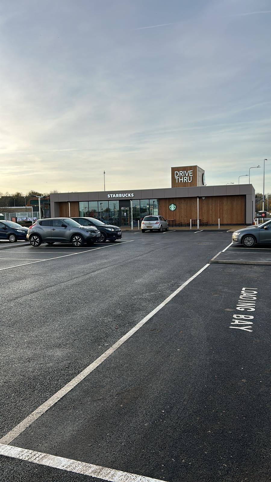 Parking lot outside a low brick building at dusk, with parked cars and a cloudy sky
