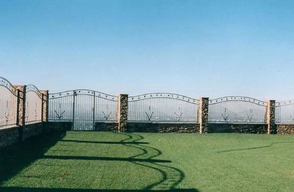 A fence with a gate in the middle of a lush green field.