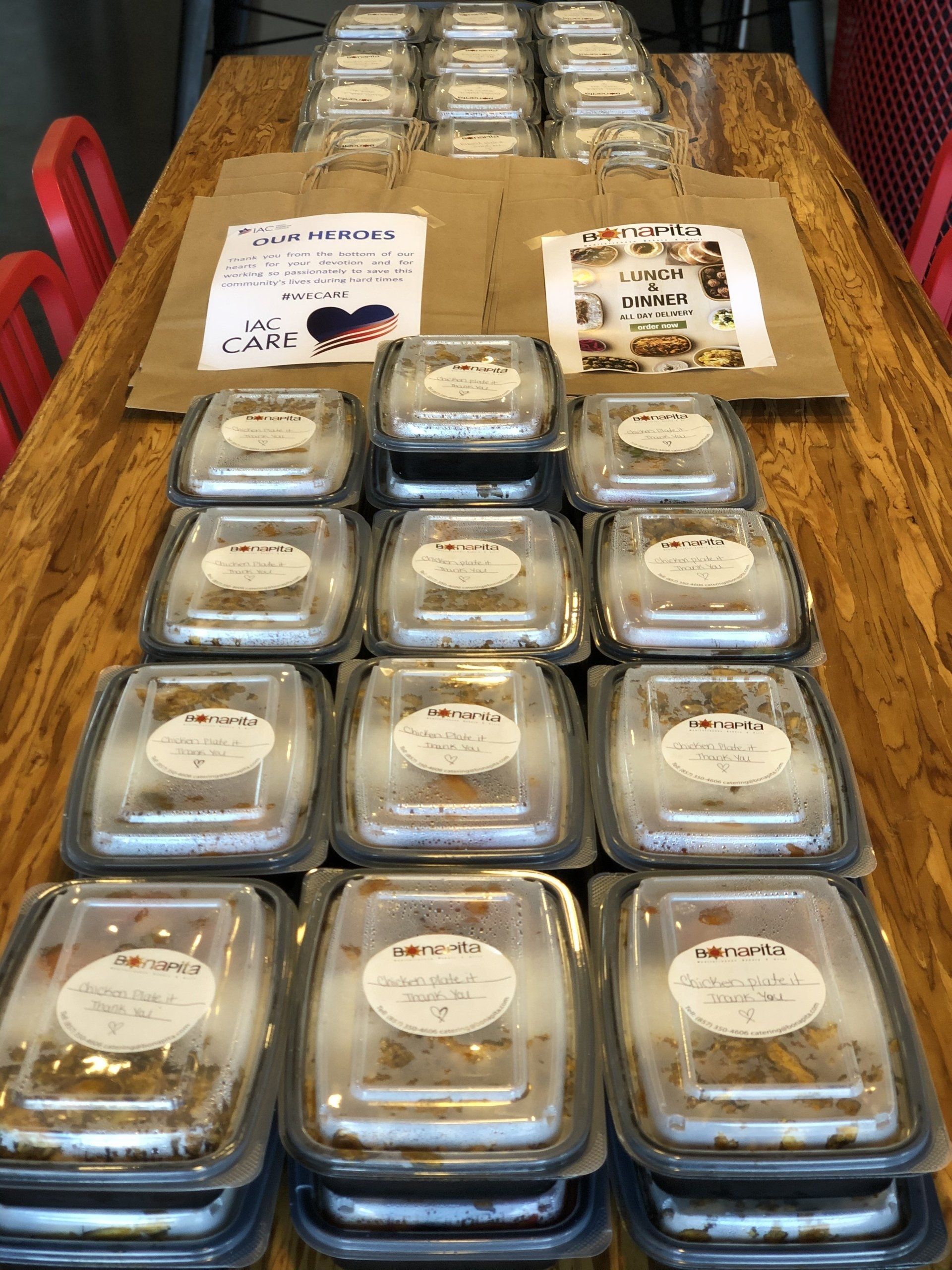 Brown table with stacks of clear containers filled with food. Two paper signs are on the table.