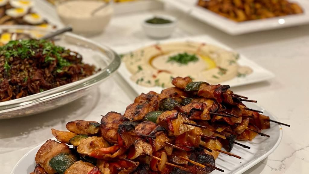 Skewered grilled chicken and vegetables on a plate, surrounded by various Middle Eastern dishes.