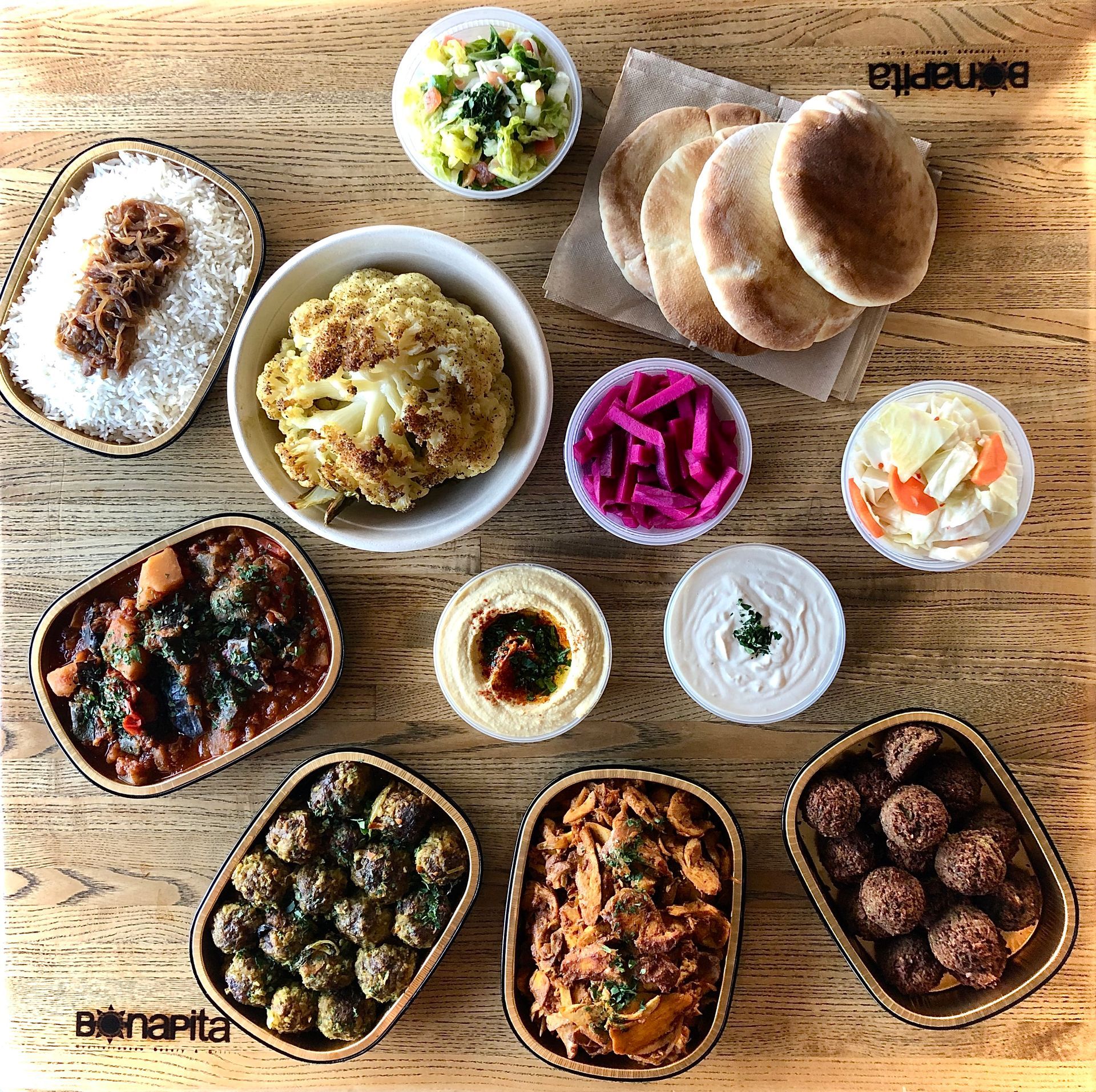Overhead shot of various Middle Eastern dishes: rice, roasted cauliflower, hummus, falafel, and pita bread.