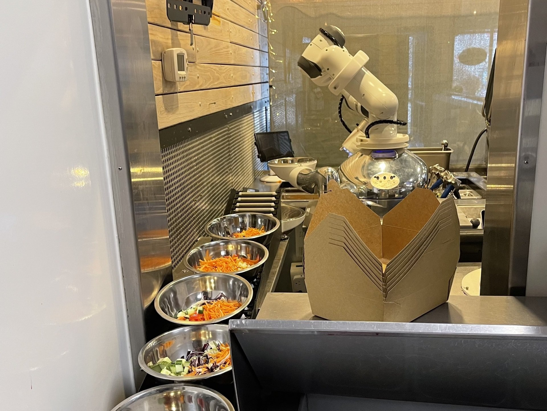 Robot arm preparing food in a commercial kitchen with bowls of ingredients.