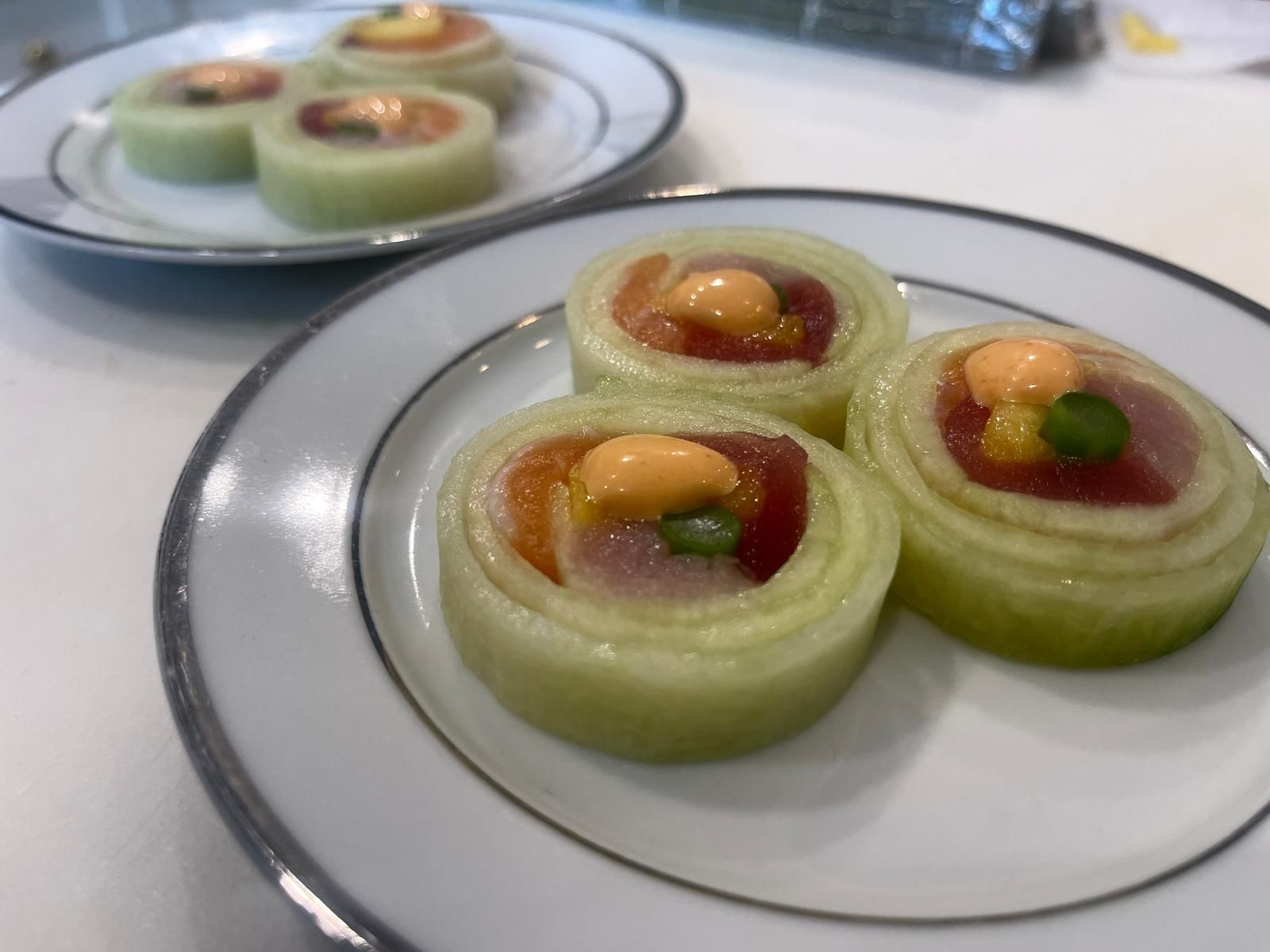 Cucumber sushi rolls with tuna and sauce on a white plate with a silver rim.