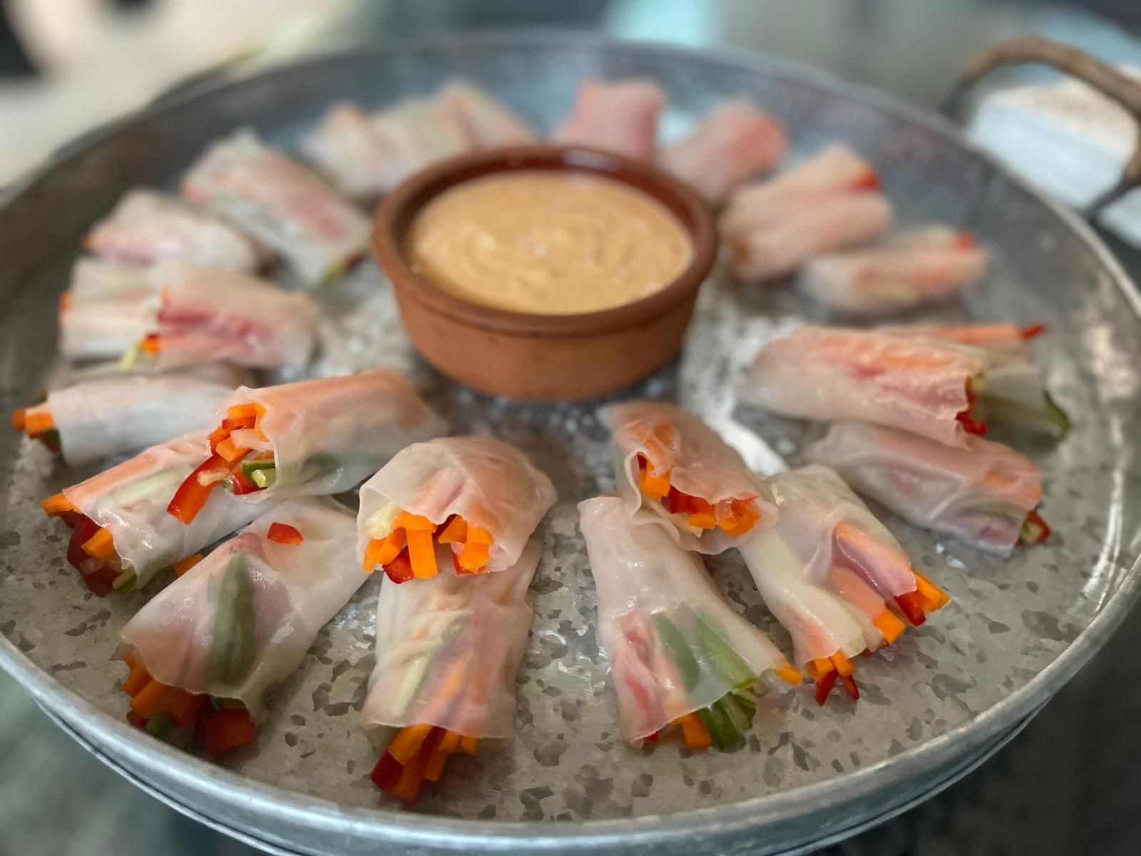 Spring rolls with colorful vegetables and dip on a metal tray.