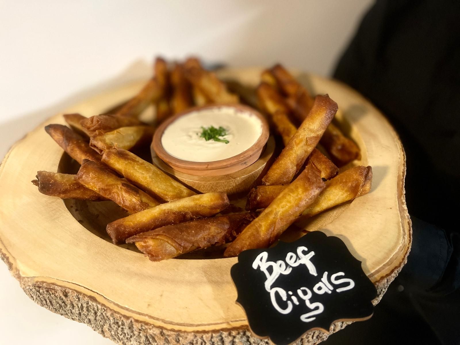 Beef cigars with dipping sauce served in a wooden bowl.