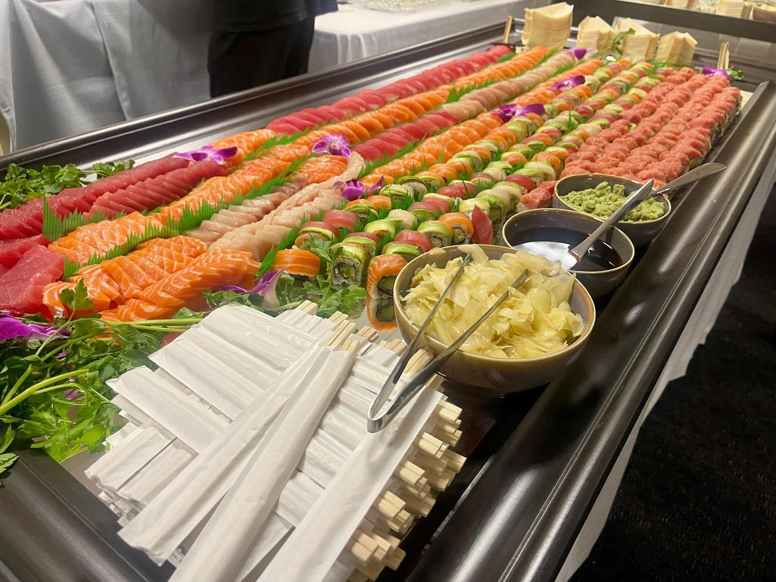 Sushi buffet with various rolls, sashimi, wasabi, soy sauce, and chopsticks.