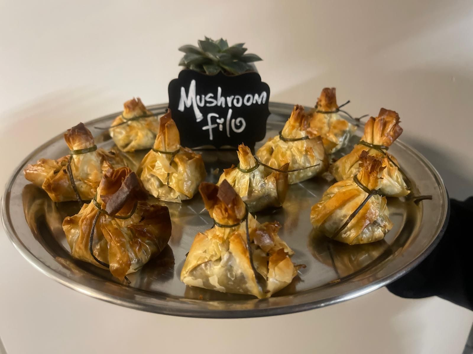 Silver tray with ten mushroom filo purses tied with green onion. A sign reads