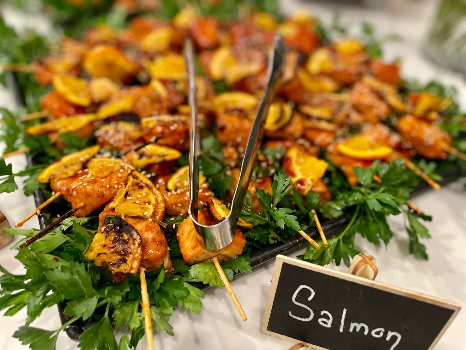 Salmon skewers with orange slices, garnished with parsley, on a platter.