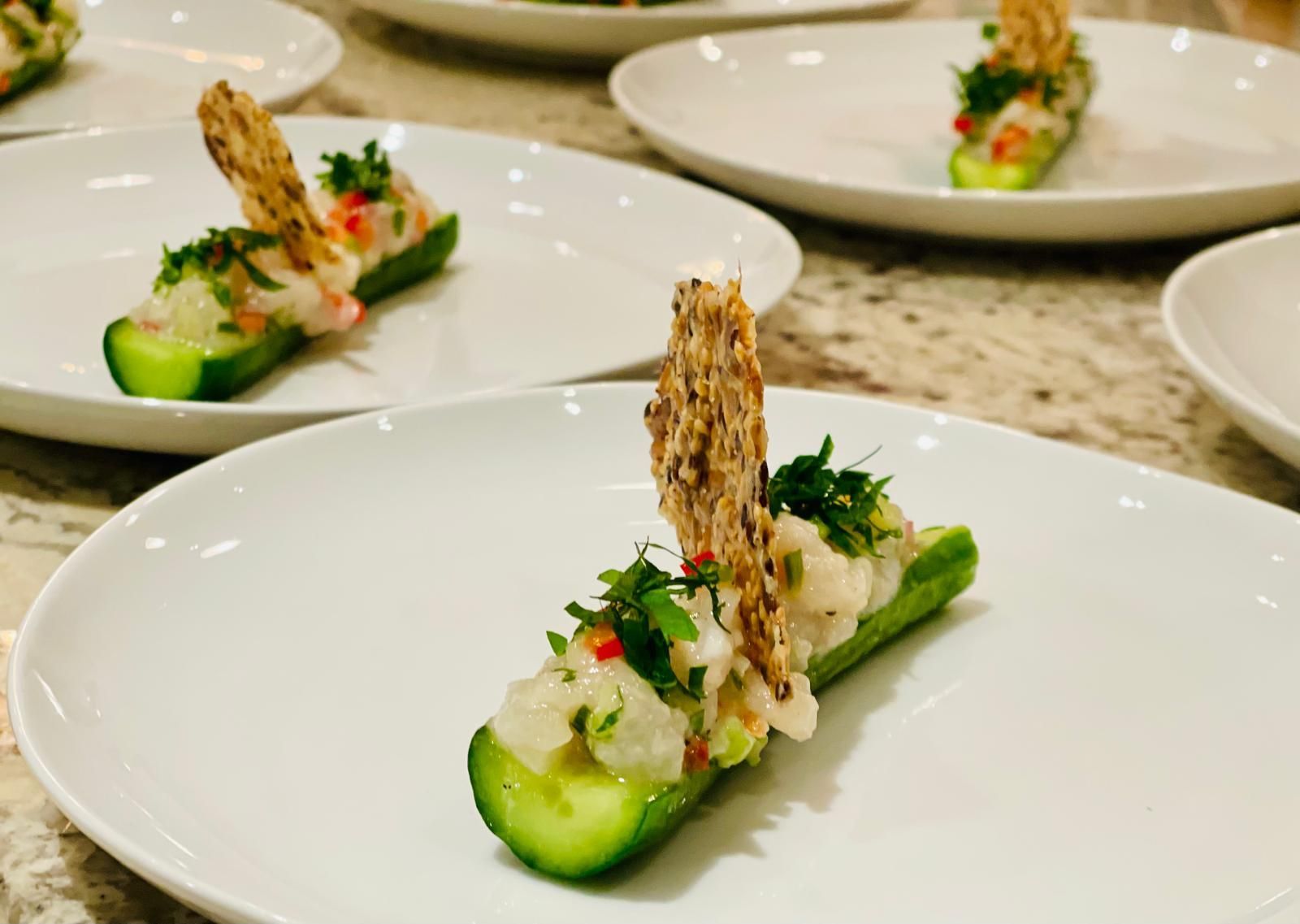 Cucumber bites topped with white mixture and cracker garnish on white plates.