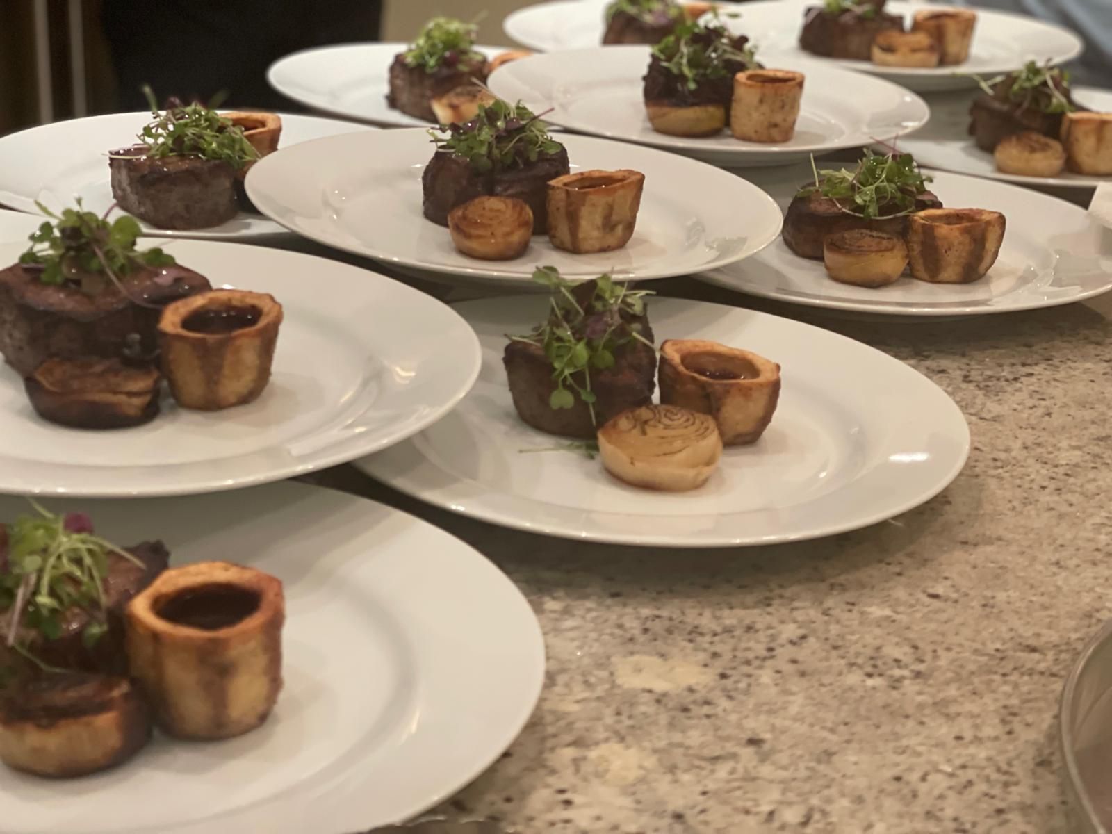 Plates of prepared food. Each has a meat portion, garnish, and a side of pastry.
