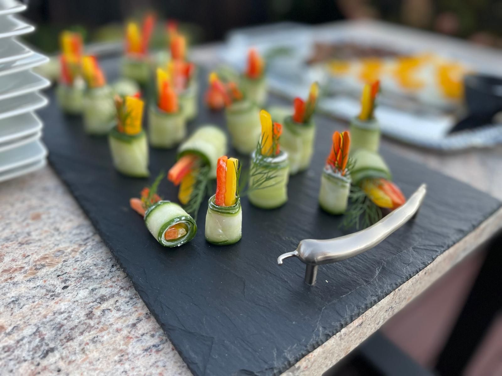 Cucumber roll appetizers with colorful pepper strips on a slate board.