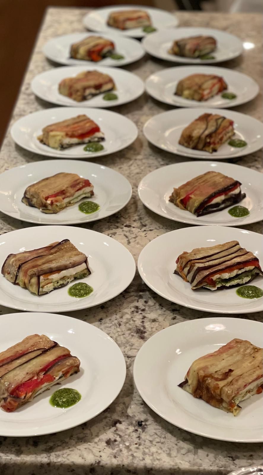 Plated eggplant stacks with layers of vegetables and a dollop of green sauce, arranged in rows on a countertop.
